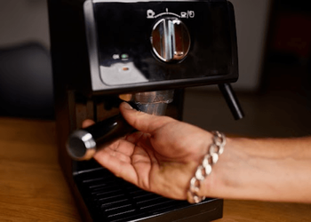 Person filling brewed coffee in cup directly from a coffee maker