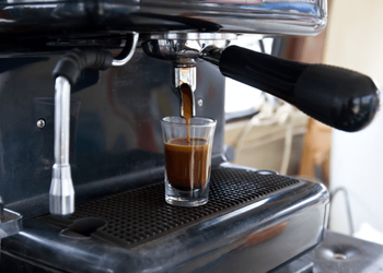 Espresso machine is filling freshly brewed espresso in a small glass