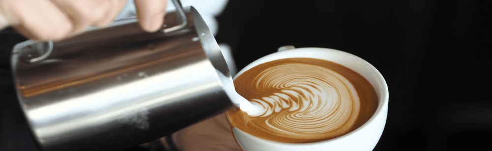 Barista designing latte art by pouring frothed milk from stainless steel frother