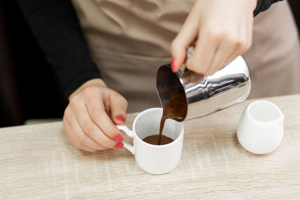 Woman pouring espresso from mug to white cup