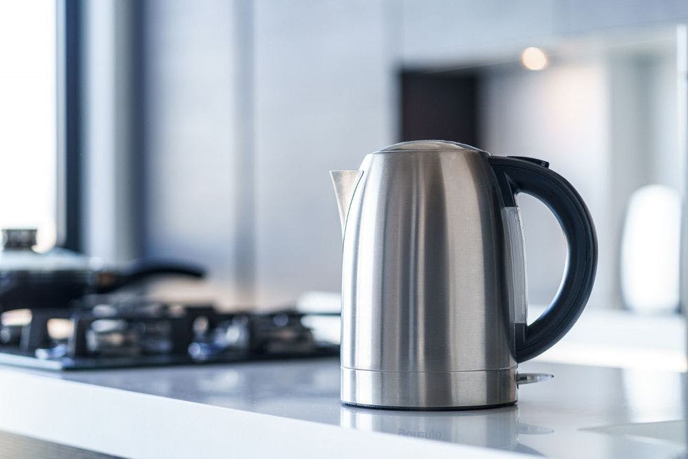 A stainless steel stovetop percolator is placed on the kitchen platform