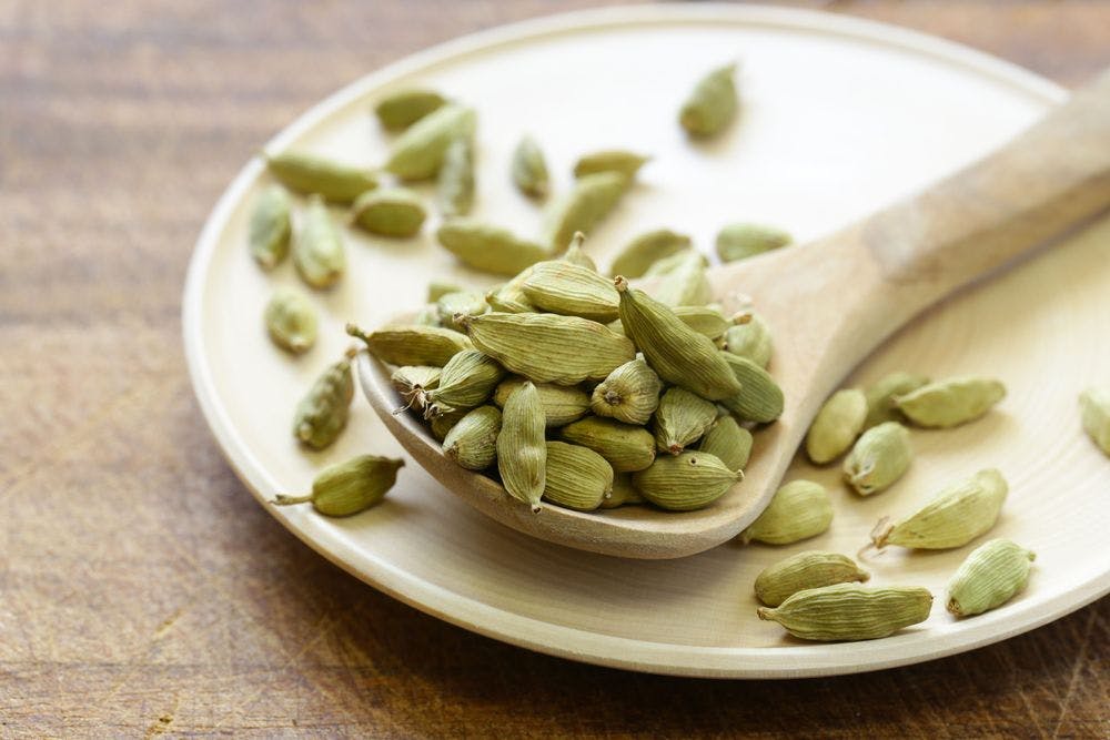 Green whole cardamom placed on the wooden spoon