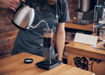 Barista pouring hot water while brewing Aeropress coffee